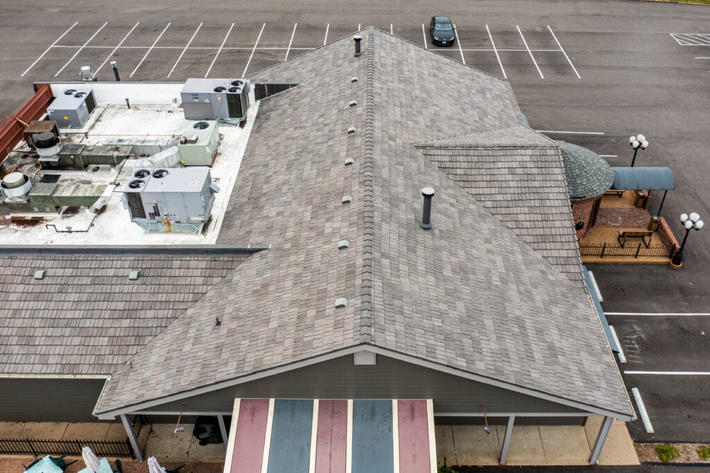 aerial-drone-view-of-a-commercial-hybrid-roof-system-featuring-grey-architectural-shingles-and-a-white-flat-membrane-section.