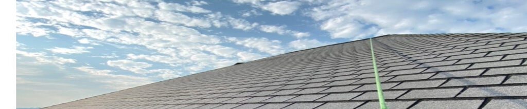 low-angle-view-of-a-grey-architectural-shingle-roof-meeting-a-blue-sky-with-clouds-